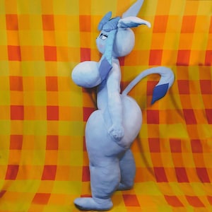 May include: A light blue plush toy with large features, including a long tail and ears. The toy is set against a yellow and orange checkered background. The plush has a cartoonish design.