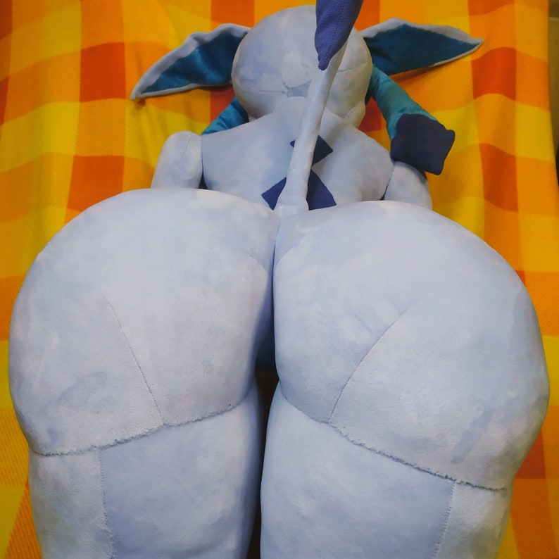 May include: A light blue plush toy with large, rounded legs and a tail. The toy has a light blue body with darker blue accents on the ears, arms, and tail. The plush is resting on a yellow and orange plaid surface.