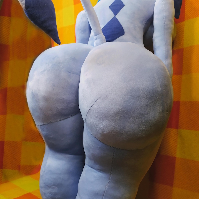 May include: A light blue plush toy, featuring a large, rounded form. The toy has a soft, textured appearance, with visible seams and a contrasting darker blue diamond pattern. The background is a plaid pattern in orange and yellow.