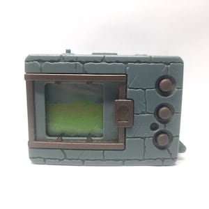 May include: A gray and brown plastic handheld electronic game with a screen that displays a green field. The game has three buttons on the right side.