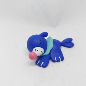 May include: A blue and teal Pokemon figurine of a seal-like creature with a pink nose and white eyes. The figurine is lying on its side with its head resting on its front flipper.