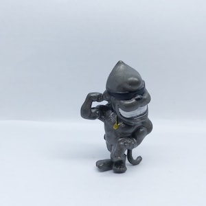 May include: A gray plastic toy monkey figurine wearing sunglasses and a gold chain. The monkey is flexing its bicep and has a mischievous grin.