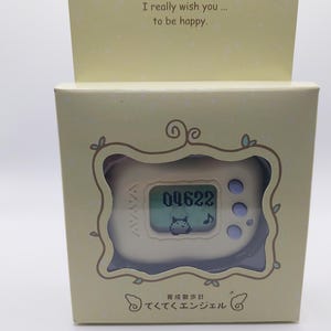 May include: A white plastic pedometer with a digital display showing the number "04622". The pedometer has a cartoon cat on the screen and is labeled "teku teku angel" and "育成散歩計 てくてくエンジェル".