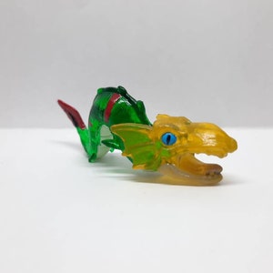 May include: A green and yellow plastic toy dragon with red accents. The dragon has a long tail and a large head with a toothy mouth and blue eyes.