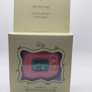 May include: A pink and yellow digital pet toy with a screen displaying "04622" and a small cat icon. The toy is in a box with the text "teku teku angel" and "育成散歩計 てくてくエンジェル" on it.