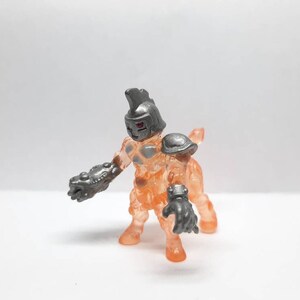 May include: A translucent orange and silver toy figure with a horned helmet and articulated arms and legs.