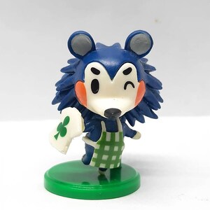 Peut inclure: Une figurine d'animal bleue et blanche portant un tablier à carreaux verts et blancs. La figurine tient une carte blanche avec un trèfle dessus. La figurine est debout sur une base verte.