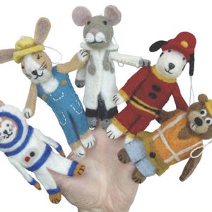 May include: A hand holding five felt finger puppets. The puppets are shaped like a bunny, mouse, dog, bear, and monkey, each wearing a costume. The bunny wears overalls, the dog a firefighter uniform, and the bear a construction worker outfit.