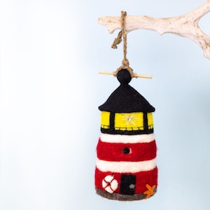 May include: A felt lighthouse ornament with red and white stripes, a yellow window, and a black roof. It has a small life preserver and a starfish on the bottom.