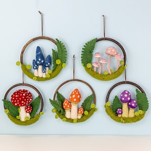 May include: Five felt mushroom wreaths with green leaves and brown wooden hoops. Each wreath features different colored mushrooms with white spots.