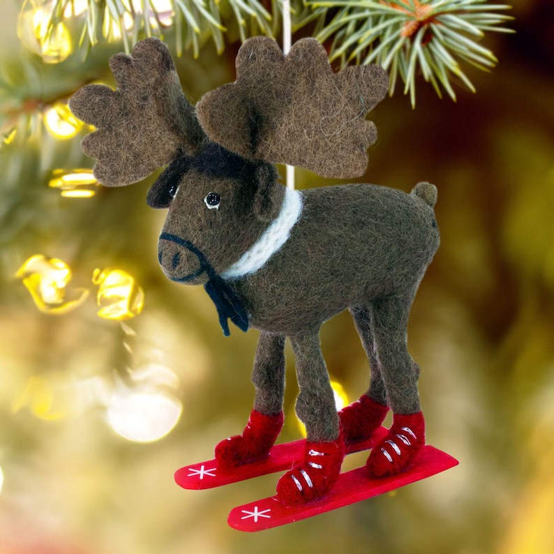 May include: A brown felt moose ornament wearing a white collar and black bow tie, skiing on red skis with white snowflakes.