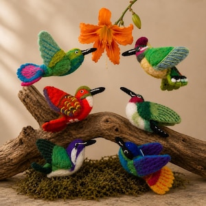 May include: A collection of colorful, handcrafted hummingbird ornaments. Each bird features vibrant hues of green, red, blue, and purple, with black beaks and intricate detailing. They are arranged on a wooden branch with an orange flower in the background.