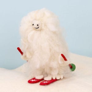May include: A white felt snowman ornament with a smiling face, wearing red ski boots and holding red skis.