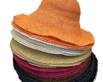 May include: A stack of straw sun hats in various colors, including orange, white, beige, pink, brown, and black. The hats are all floppy and have a wide brim.
