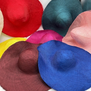 Puede incluir: Una colección de sombreros de sol de ala ancha en varios colores, incluyendo rojo, azul, rosa, amarillo y verde. Los sombreros tienen una textura tejida y un diseño clásico y flexible, ideal para la protección solar y la moda.