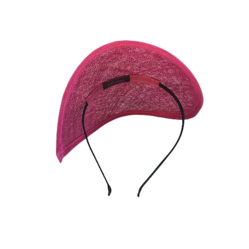 Puede incluir: Una diadema de tela rosa con un borde curvo y una banda el&aacute;stica negra. La diadema tiene una peque&ntilde;a etiqueta que dice "Hatloom".