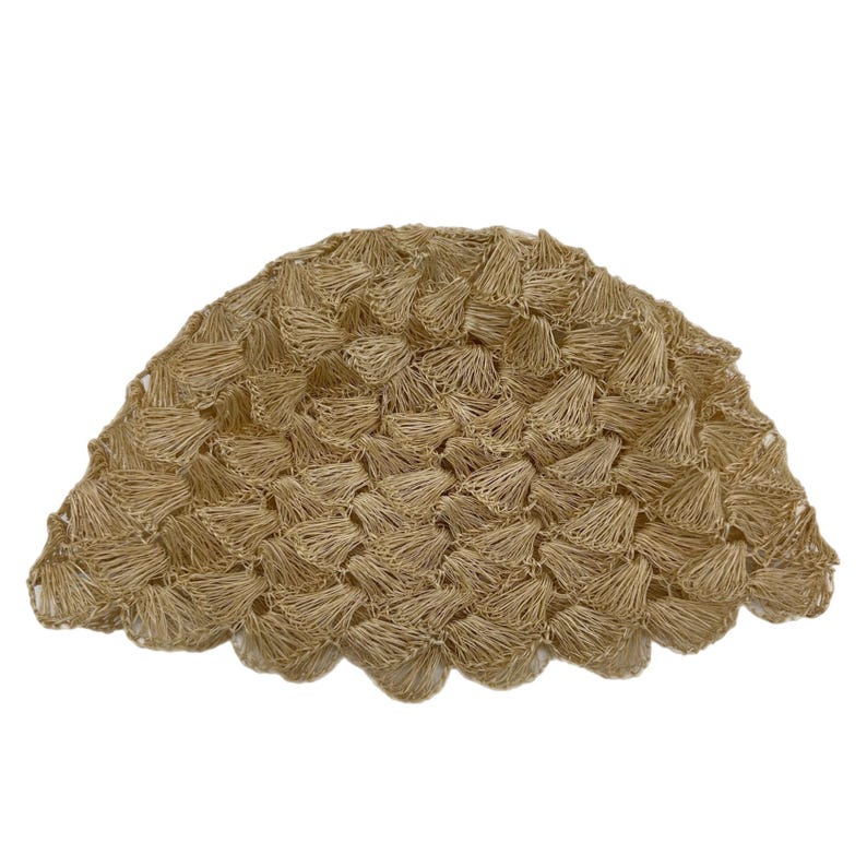 May include: A woven, beige, half-circle shaped decorative object. The object is made of tightly woven, small, cone-shaped pieces. The edges have a scalloped design. The background is white.