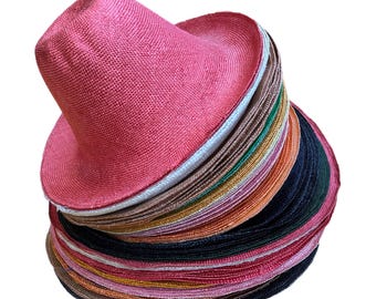 May include: A stack of straw hats in various colors, including pink, brown, green, and black. The top hat is a bright pink color.