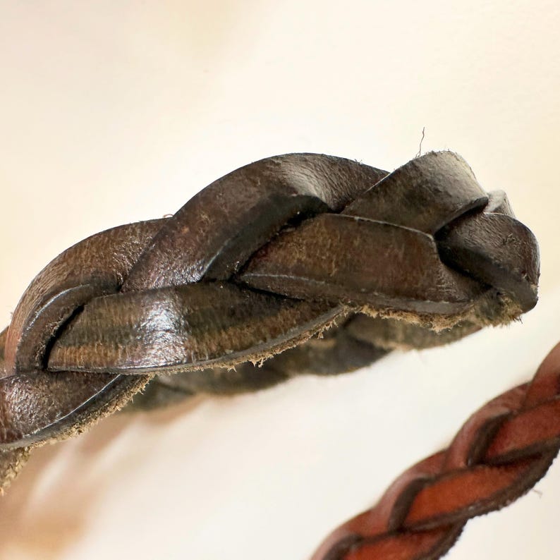 May include: Close-up of a brown leather braided strap. The strap is woven in a tight pattern and has a slightly worn look.