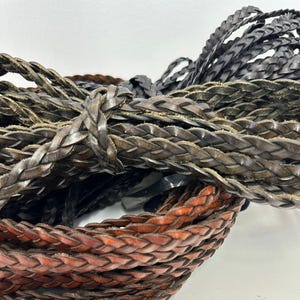 May include: Close-up of two braided leather cords, one brown and one dark gray. The cords are woven together in a tight, intricate pattern.