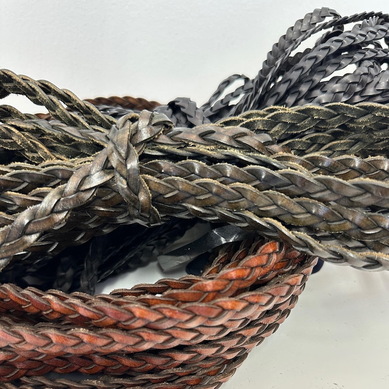 May include: Close-up of two braided leather cords, one brown and one dark gray. The cords are woven together in a tight, intricate pattern.