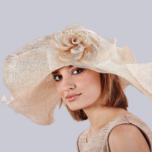 Peut inclure: Un grand chapeau beige souple avec une grande fleur beige sur le côté. Le chapeau est fait d'un matériau tissé et a une large bordure.