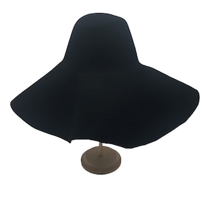 May include: A wide-brimmed black felt hat with a rounded crown. The hat is displayed on a wooden stand.