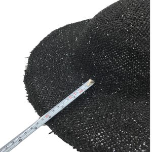 May include: Black straw hat with silver glitter woven into the fabric. The hat is measured with a tape measure.
