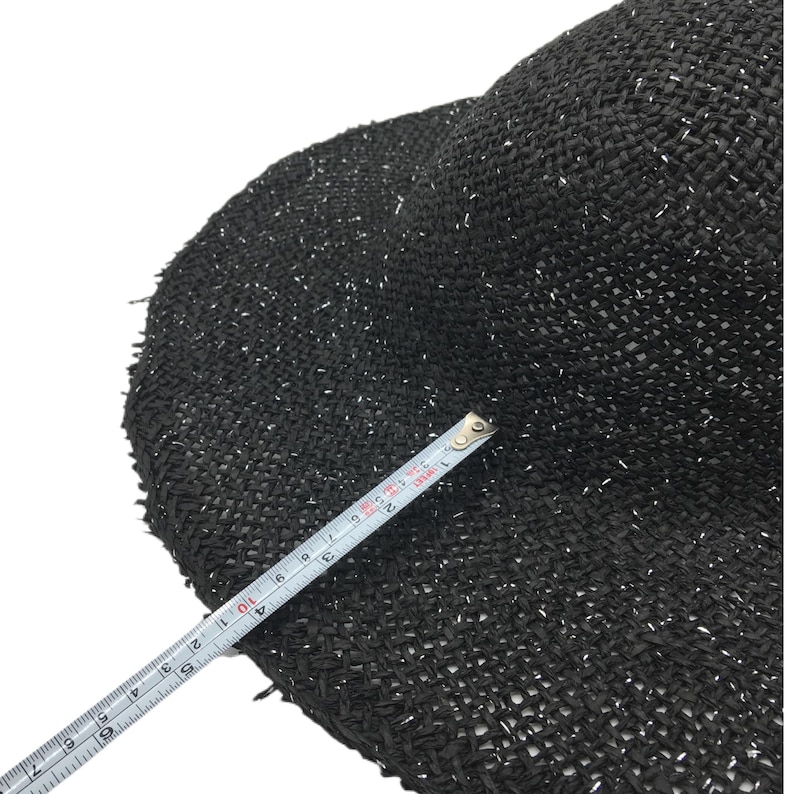 May include: Black straw hat with silver glitter woven into the fabric. The hat is measured with a tape measure.