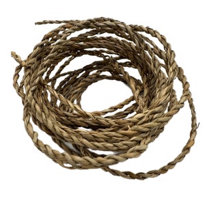 May include: Coiled natural fibre rope. The rope is a light brown colour and appears to be made of woven strands. The rope is tightly wound in a circular pattern, with the end of the rope visible at the top and right side of the image.