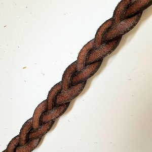 May include: Close-up of a brown leather cord braided in a complex pattern.