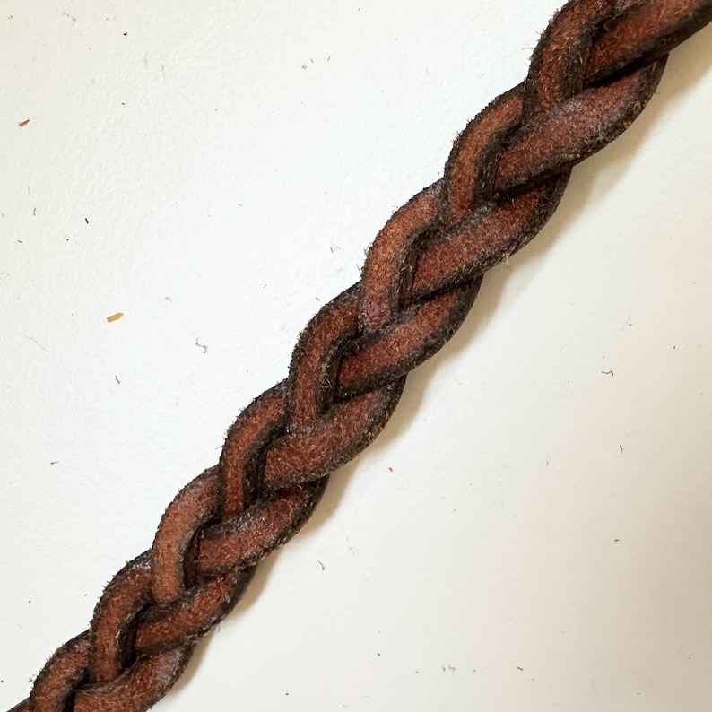 May include: Close-up of a brown leather cord braided in a complex pattern.