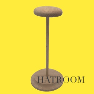 May include: A wooden hat stand with a round top and a tall, slender base. The stand is made of light brown wood and has a smooth finish.