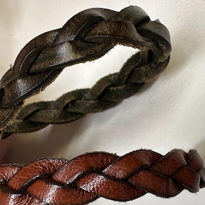 May include: Two braided leather straps, one brown and one dark brown. The straps are woven together in a simple braid pattern.