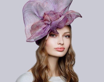 May include: A purple and pink formal hat with a large floral accent. The hat is made of a sheer, woven material and features a wide brim and a decorative flower on top. The hat is a stylish accessory for special occasions.