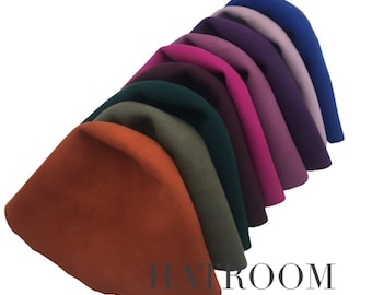 May include: A stack of eight felt hats in various colors, including orange, green, burgundy, pink, purple, lavender, and blue. The hats are arranged in a semi-circle, with the orange hat at the bottom and the blue hat at the top. The hats are all made of a soft, felted material and have a simple, classic design. The text "HATROOM" is visible at the bottom of the image.