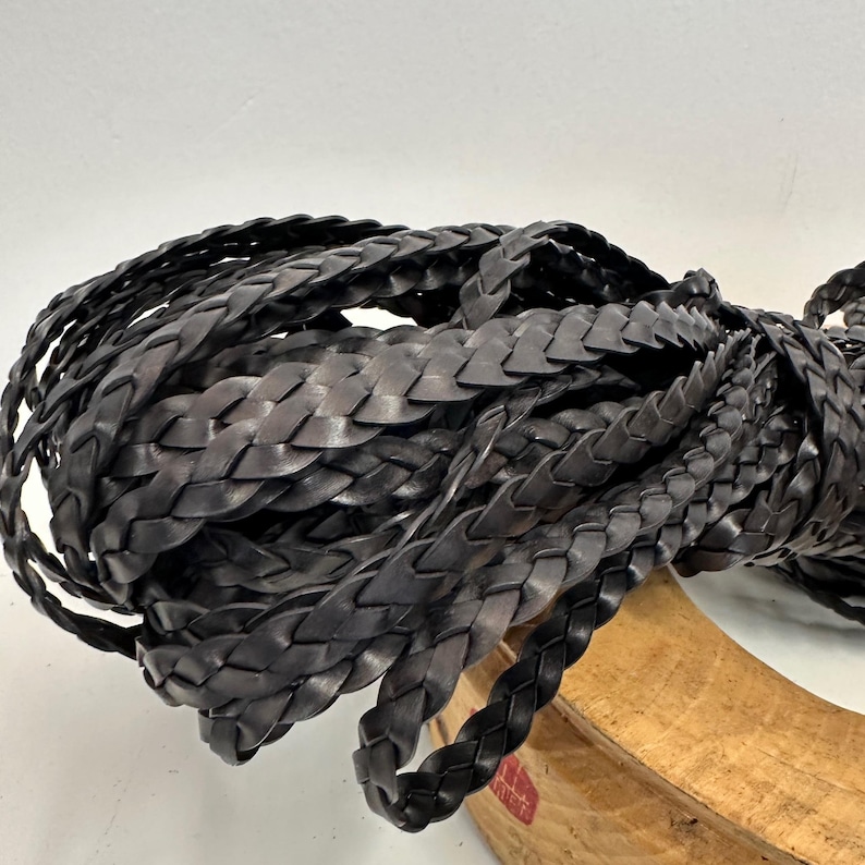 May include: A close-up of a pile of black braided leather cord. The cord is thick and has a woven texture.