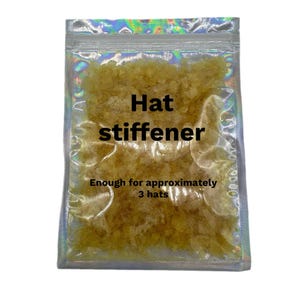 May include: A clear, holographic-finish resealable pouch containing yellow, granular hat stiffener. The text on the pouch reads: Hat stiffener. Enough for approximately 3 hats. The contents are small, irregular, translucent yellow flakes.