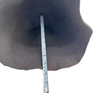 Może przedstawiać: Ciemnoszary kapelusz z szerokim rondem, mierzony miarką. Miarka pokazuje, że kapelusz ma średnicę około 28 cm. Kapelusz jest wykonany z miękkiego materiału i jest umieszczony na białym tle.