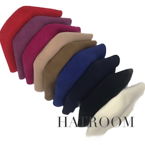 Może przedstawiać: Kolekcja dziesięciu filcowych beretów w różnych kolorach, w tym czerwony, fioletowy, różowy, beżowy, brązowy, niebieski, granatowy i biały. Berety są ułożone wachlarzowo, z białym beretem na dole.