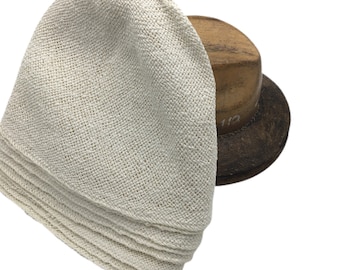 May include: A stack of off-white, textured, woven fabric squares with visible cross-hatch patterns. The fabric is folded in layers, displaying a consistent, coarse weave throughout each piece. The material appears light in color and uniform in its construction.