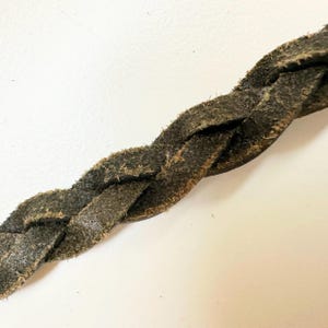 May include: Close-up of a dark green braided leather cord.