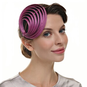 Könnte beinhalten: Ein magenta-farbenes Kopfstück mit Spiraldesign. Das Kopfstück besteht aus geschichtetem, strukturiertem Material und hat eine kleine, runde Verzierung. Das Accessoire wird an der Seite des Kopfes getragen.