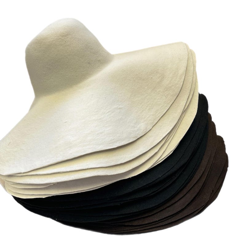 May include: A stack of hat forms in three colors: white, black, and brown. The forms are made of a soft, pliable material and are designed to be used for shaping hats.