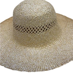 May include: A wide-brimmed straw hat in a natural, light beige hue. The hat has a woven construction with a perforated band around the crown. The brim is wide, offering good sun protection. Ideal for sunny days, this hat is a summer essential.