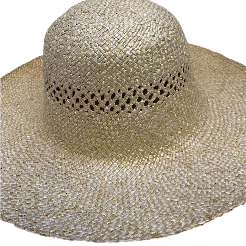 May include: A wide-brimmed straw hat in a natural, light beige hue. The hat has a woven construction with a perforated band around the crown. The brim is wide, offering good sun protection. Ideal for sunny days, this hat is a summer essential.