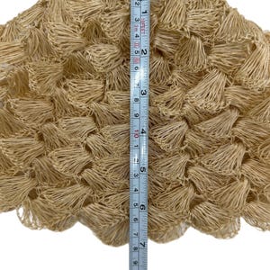 May include: Close-up of a beige, textured fabric with a fringe-like design. The fabric is approximately 20 cm in length, as measured by a ruler. The material appears to be woven or crocheted, with a dense, three-dimensional texture.