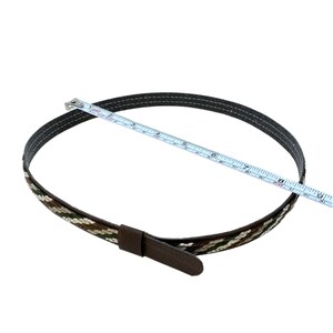 K&ouml;nnte beinhalten: Ein brauner Lederg&uuml;rtel mit einem gewebten Muster in Braun, Wei&szlig; und Gr&uuml;n. Der G&uuml;rtel wird mit einem Ma&szlig;band gemessen und ist etwa 20 cm lang.