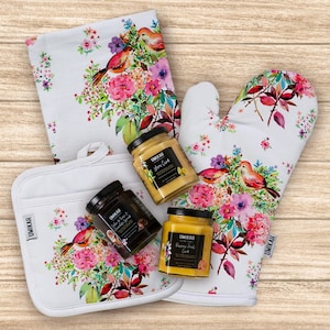 May include: A set of kitchen accessories featuring a white oven mitt, a white pot holder, and three glass jars of preserves. The oven mitt and pot holder have a floral pattern with birds. The jars are labeled "Lemon & Ginger Curd", "Salted Caramel & Chocolate Spread", and "Passion Fruit Curd".