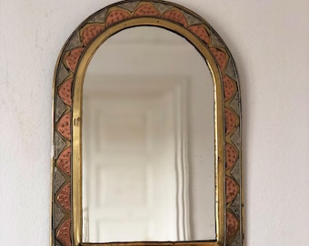May include: An arched wall mirror featuring a decorative metal frame with a brass-toned inner border and a wider outer border. The outer border displays a repeating pattern of copper-colored semi-circles set against a textured silver-toned background.